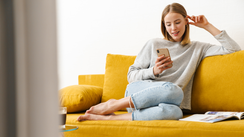 A woman sits on her couch shopping on her phone